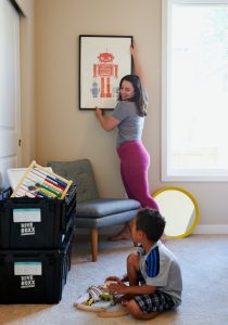 A woman taking down a picture frame from the wall while looking at a child who watches