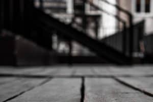 A gap between wooden floor boards shown against a blurry flight of stairs