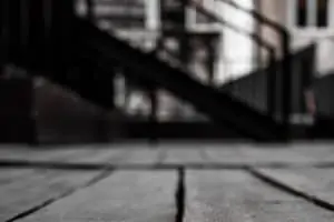 A gap between wooden floor boards shown against a blurry flight of stairs