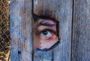 A man’s eye showing through a hole on a wooden fence