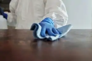 A close-up of the hand of a person in protective suit who is wiping a chemical on a wooden surface