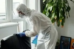 A person in protective suit inspecting and spraying a solution on a black couch