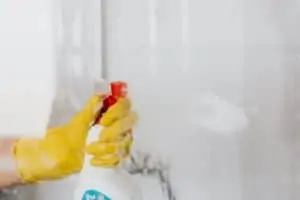 A hand wearing a glove and spraying a cleaning solution on a clear glass
