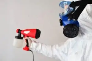 A person in protective clothing holding a disinfecting spray equipment