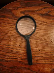 A black magnifying glass on top a brown, wooden surface