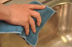 A close-up of a hand wiping a wet sink with an old, used hand towel