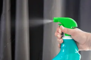 A hand spraying a plastic spray bottle on grey curtains.