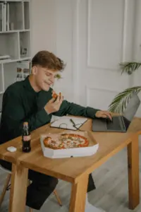 A man eating pizza on a wooden work table inside a room