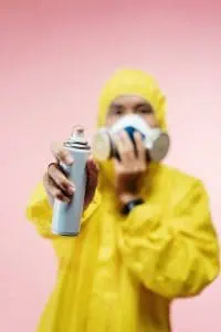 A person wearing a yellow PPE and holding a spray can.
