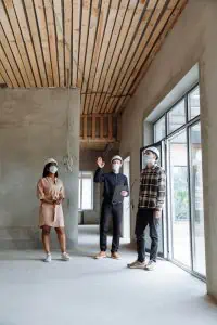 Three people wearing hard hats and face masks while looking at an unfinished wooden ceiling