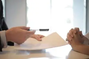 A Person Handing Pen and Paper to Another Person